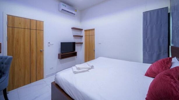 Une chambre à coucher avec un lit, un téléviseur posé sur une étagère, des armoires en bois et un luminaire au plafond.