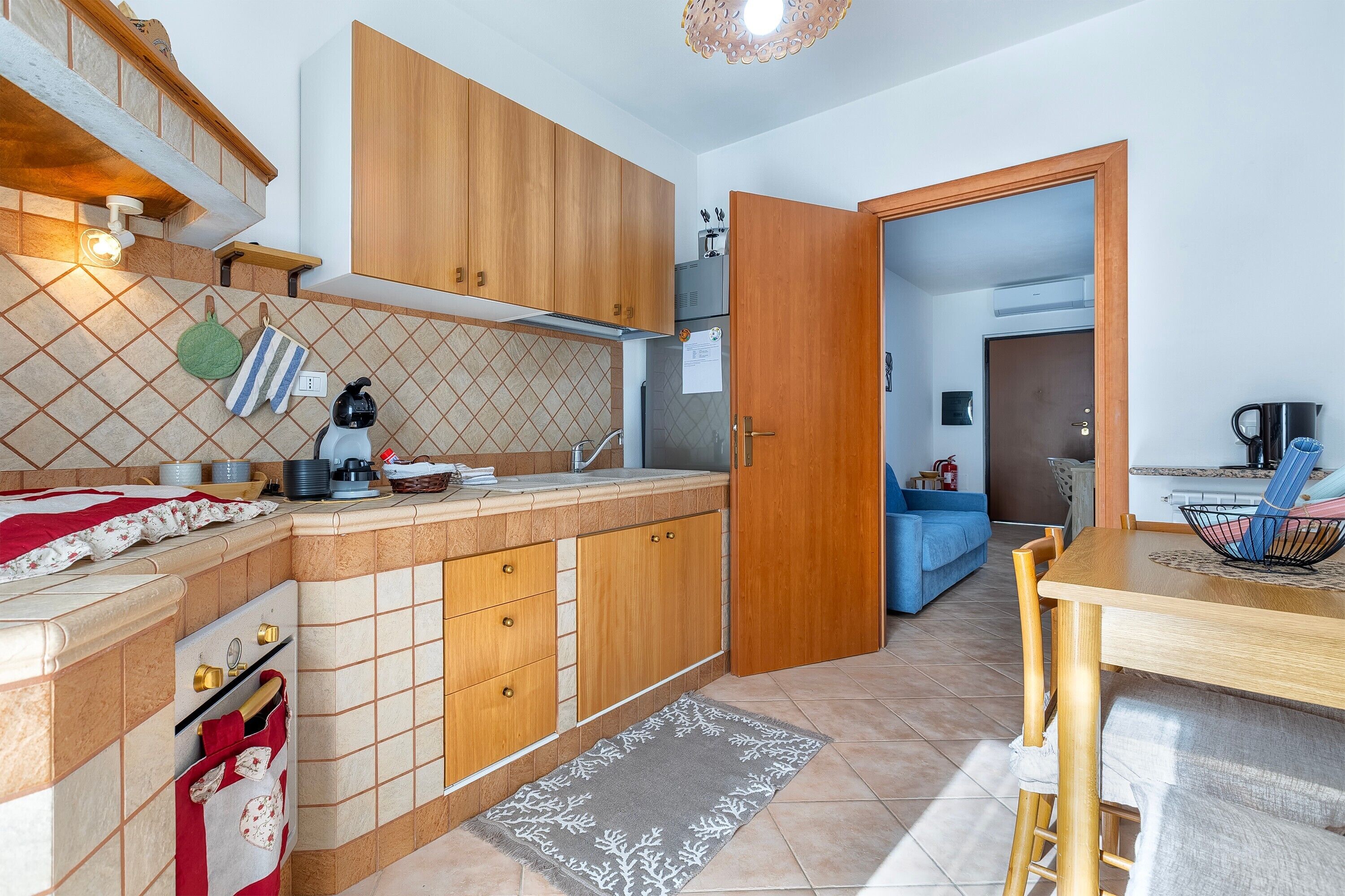 Une cuisine avec des meubles de rangement en bois, un pare-feu en carrelage, une table à manger avec des chaises, et une porte visible donnant sur une autre pièce.