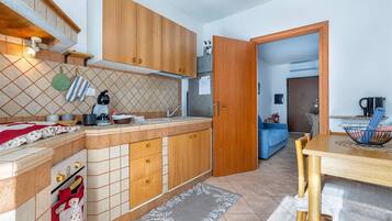 Une cuisine avec des meubles de rangement en bois, un pare-feu en carrelage, une table à manger avec des chaises, et une porte visible donnant sur une autre pièce.