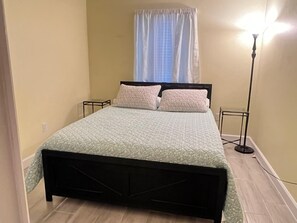 A bedroom with a bed, two bedside tables, a floor lamp, and a window with curtains. - Spacious Dunnellon House 3BR/2B  |7 Beds| Near Rainbow River (Dunnellon)