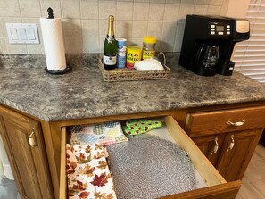 A kitchen counter with a coffee maker, a basket containing a bottle of champagne, granulated sugar, and a jar of coffee. - Spacious Dunnellon House 3BR/2B  |7 Beds| Near Rainbow River (Dunnellon)