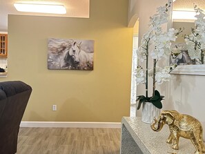 A room with a beige wall, a mounted painting of a horse, a white orchid plant, and a golden elephant statue on a textured table.