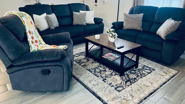Un salon avec deux canapés sombres, une table basse et un tapis à motifs.