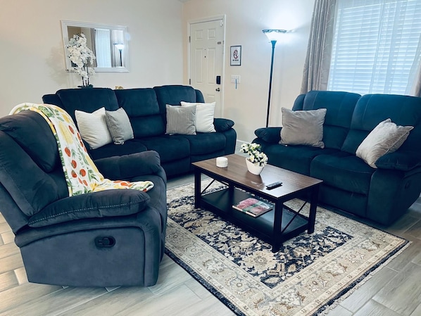 A living room with two dark sofas, a coffee table, and a patterned rug.