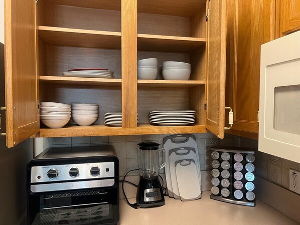 A kitchen with wooden cabinets, a Curtis Stone toaster oven, a blender, and a spice rack.