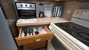 A kitchen with a Curtis Stone oven, a blender, a coffee maker, and a spice rack.