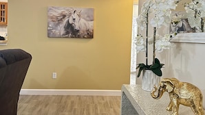 A room with a beige wall, a mounted painting of a horse, a white orchid plant, and a golden elephant statue on a textured table.