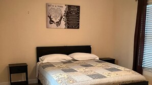 Une chambre à coucher avec un lit, deux tables de chevet, une affiche murale et une fenêtre avec des stores.