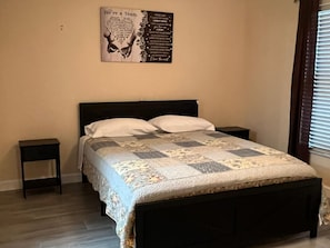 A bedroom with a bed, two bedside tables, a wall poster, and a window with blinds.