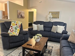 A living room with two dark sofas, a wooden coffee table, and a patterned throw blanket.