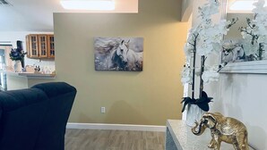 A living room with a dark-colored sofa, a painting of a horse, and a decorative elephant on a shelf.