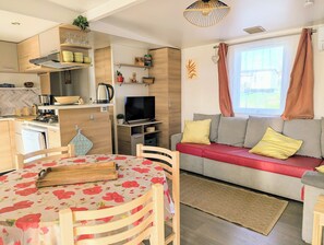 Een knus verblijf met kitchenette, een eethoek, een zithoek met een bank en kussens, en een televisie.