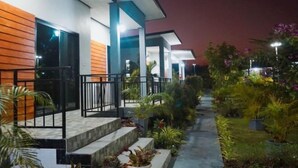 Un edificio moderno con un área exterior cubierta, escalones que conducen a la entrada y varios maceteros con plantas.