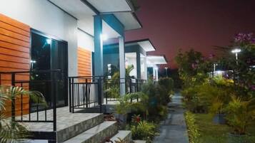 A modern building with a covered outdoor area, steps leading to a balcony, and various potted plants.