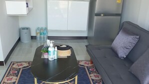 A living area with a sofa, a coffee table with toiletries, a patterned rug, and a kitchen in the background. - GuddahHomestay (Sawang Daen Din)