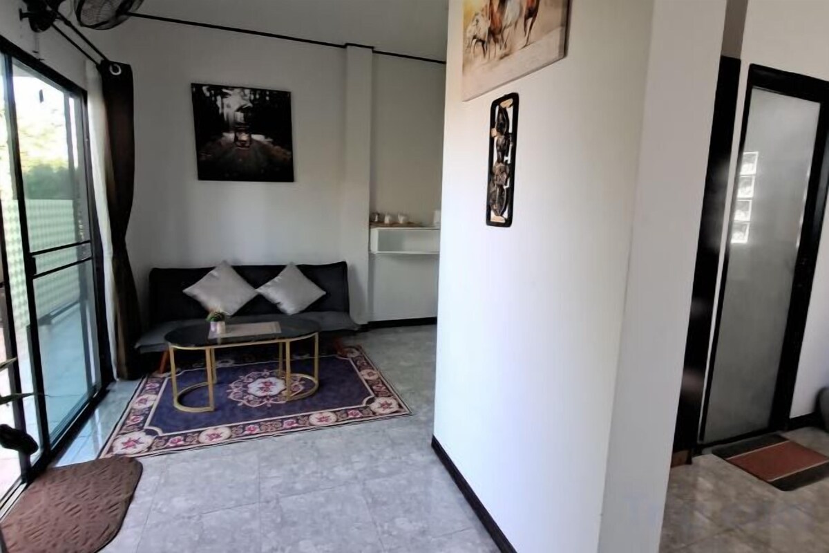 A room with a sofa, a small table, a patterned rug, a door, and a wall-mounted artwork.