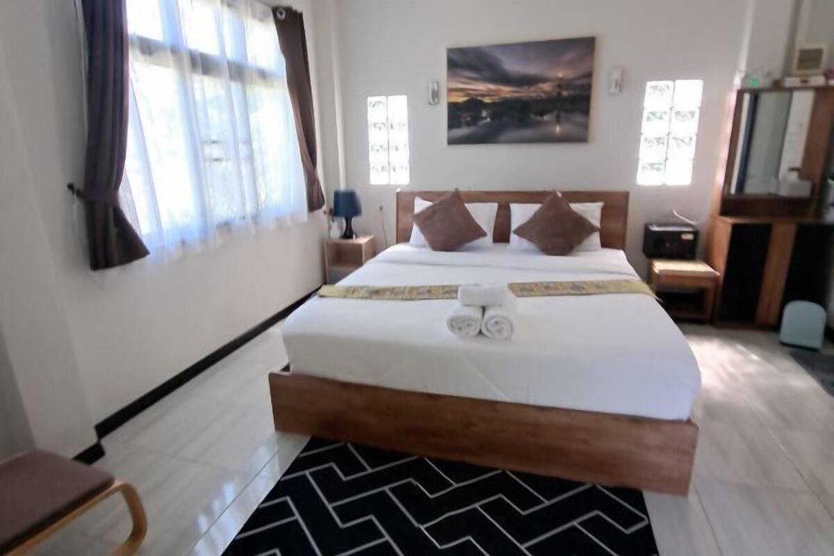 A hotel room with a bed, a nightstand, a desk, and a chair.