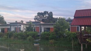 A row of modern houses with a water body in front, surrounded by greenery. - GuddahHomestay (Sawang Daen Din)