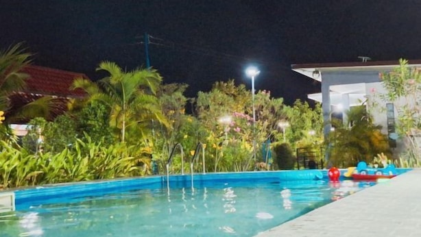 A swimming pool at night with surrounding vegetation and a building in the background. - GuddahHomestay (Sawang Daen Din)