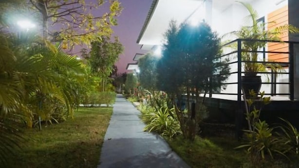 Un camino lleva a un edificio de diseño moderno, rodeado de abundante vegetación e iluminado por farolas.