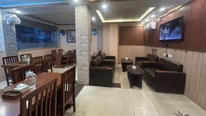 A restaurant with wooden tables and chairs, a stone pillar, and a TV mounted on the wall. - Hotel white palace airport Kathmandu  (Kathmandu)