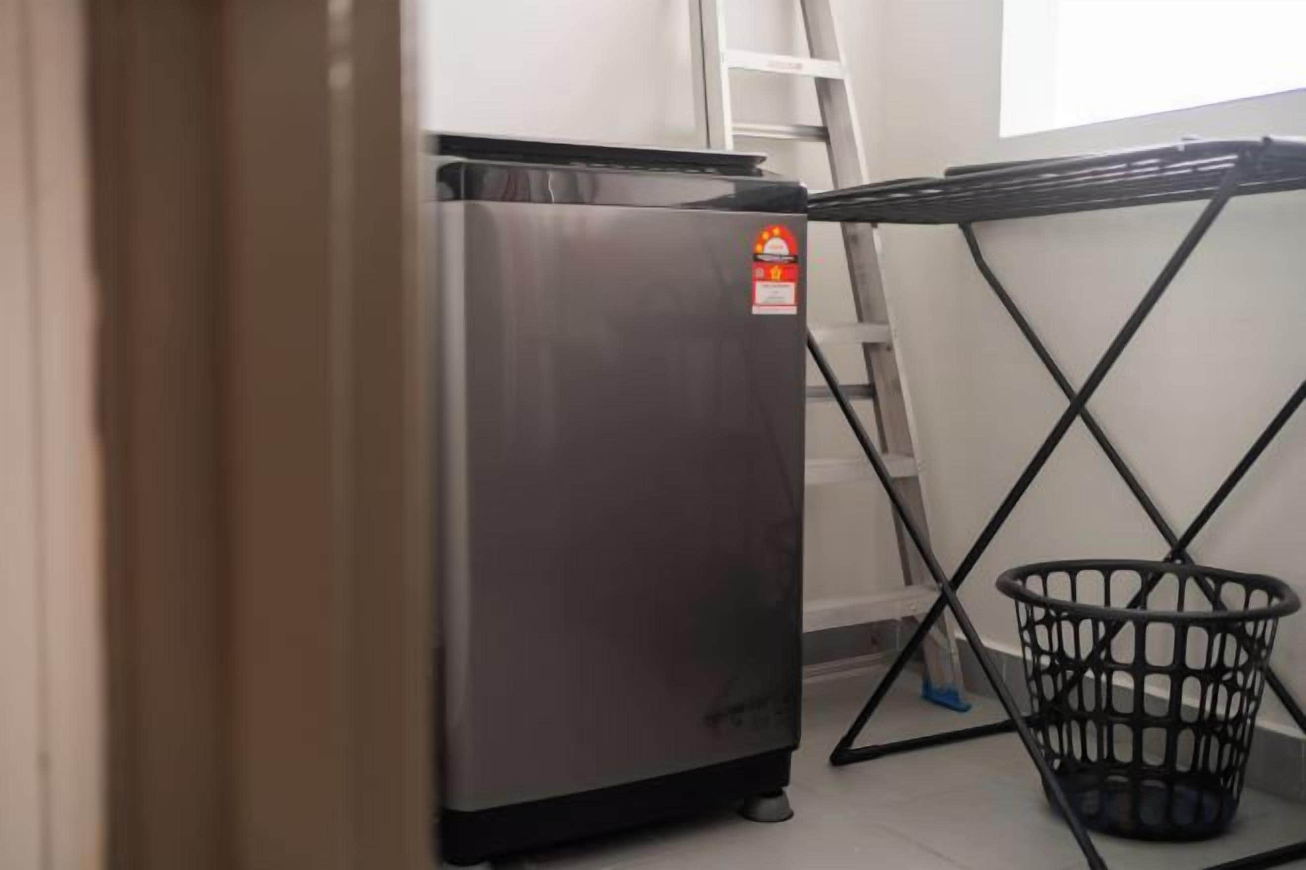 A compact kitchen area with a stainless steel refrigerator, a black metal table with a basket, and a white wall.