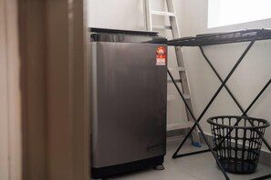 A compact kitchen area with a stainless steel refrigerator, a black metal table with a basket, and a white wall.