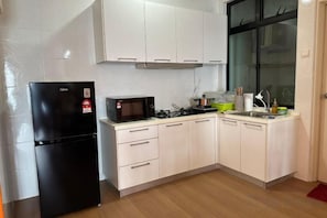A compact kitchen with a black refrigerator, a microwave, a gas stove, and white cabinets.