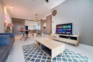 Moderni olohuone, jossa on litteänäyttöinen televisio, sohvapöytä ja sohva. Taustalla on keittiöalue, jossa on ruokapöytä ja tuolit.