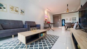 A modern living room with a grey sofa, a wooden coffee table, and a patterned rug. There is a neon sign on the wall and a ceiling fan. - The Platino Johor Bahru (Tebrau)