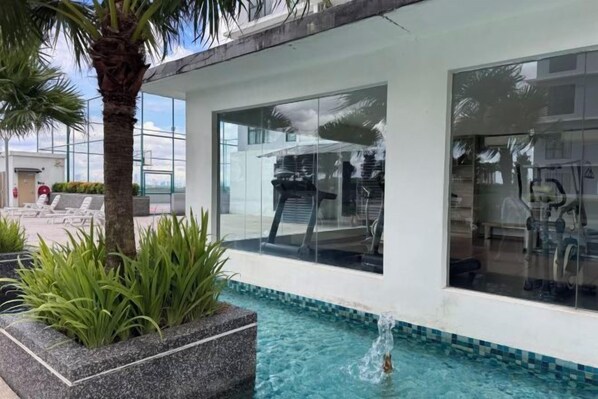 A modern pool area with clear blue water, a palm tree, and a glass-enclosed room with a view.