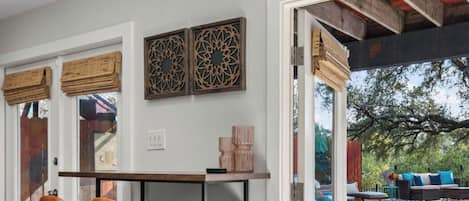 Um espaço interior com mesa e cadeiras, uma janela com persianas e vista para um pátio externo.