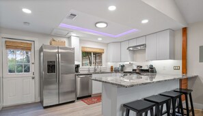 A modern kitchen with a large island, stainless steel appliances, and a view to the backyard. - Private Pool Home Near Lake Travis | Firepit, Grill & Hot Tub | Pet-Friendly! (Austin)
