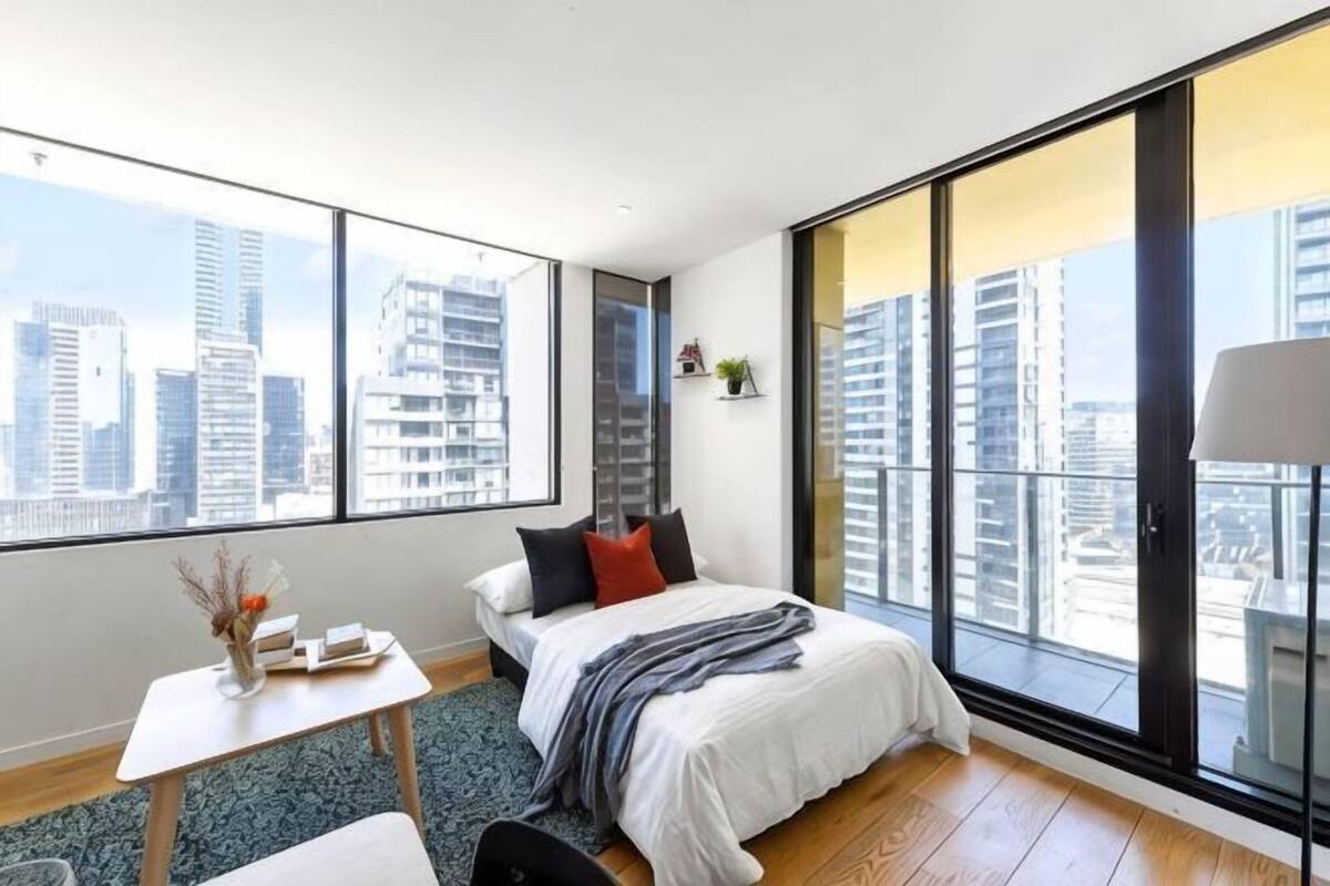 Ein modernes Schlafzimmer mit großem Fenster, einem Bett, einem kleinen Tisch und einem Stuhl.