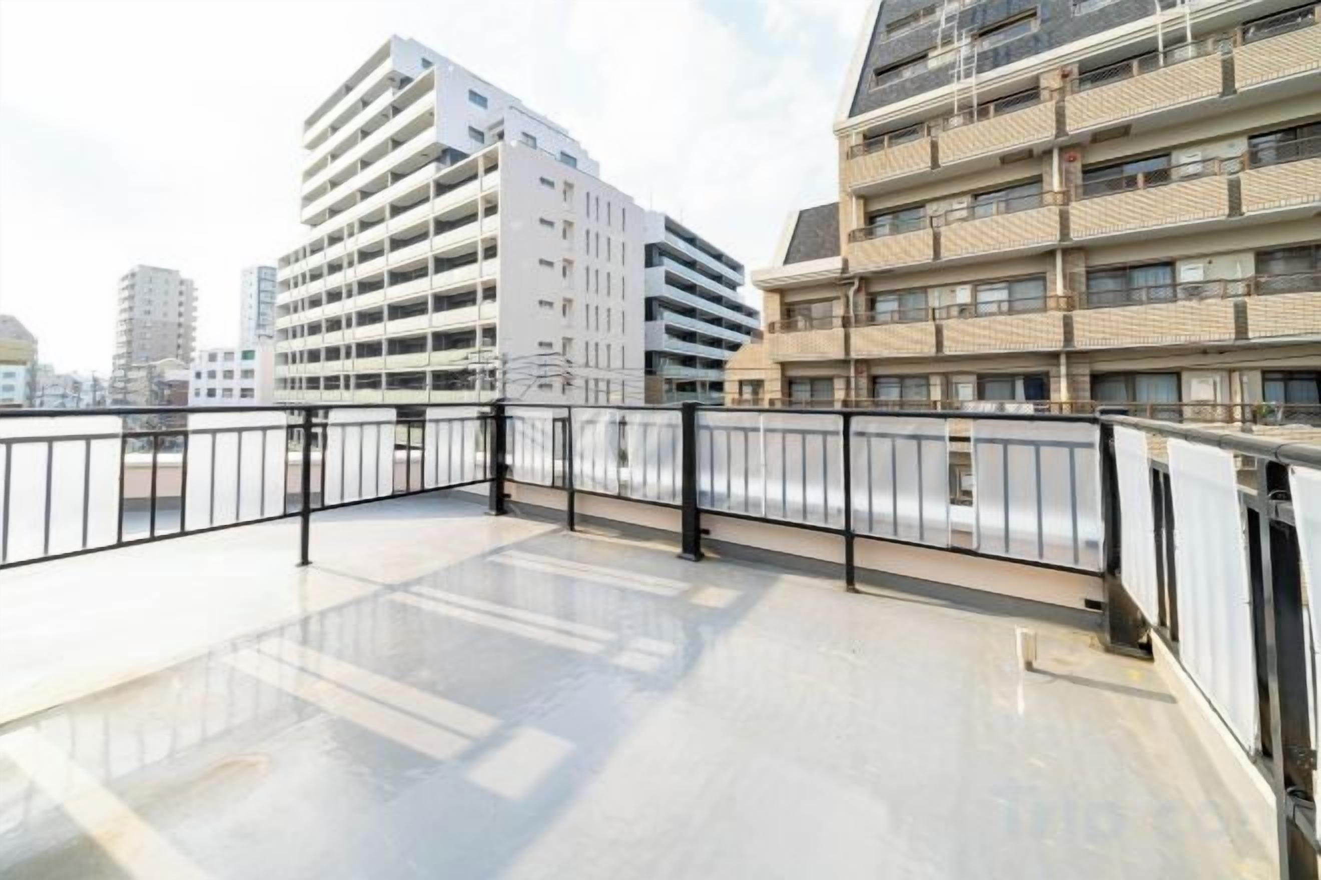 A rooftop terrace with a metal railing, a view of adjacent buildings, and a clear sky.
