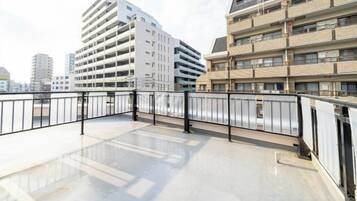 A rooftop terrace with a metal railing, a view of adjacent buildings, and a clear sky.