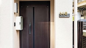 Entrada de un edificio moderno con una puerta de madera oscura, un cartel que indica la dirección y una pequeña caja de servicios en la pared.