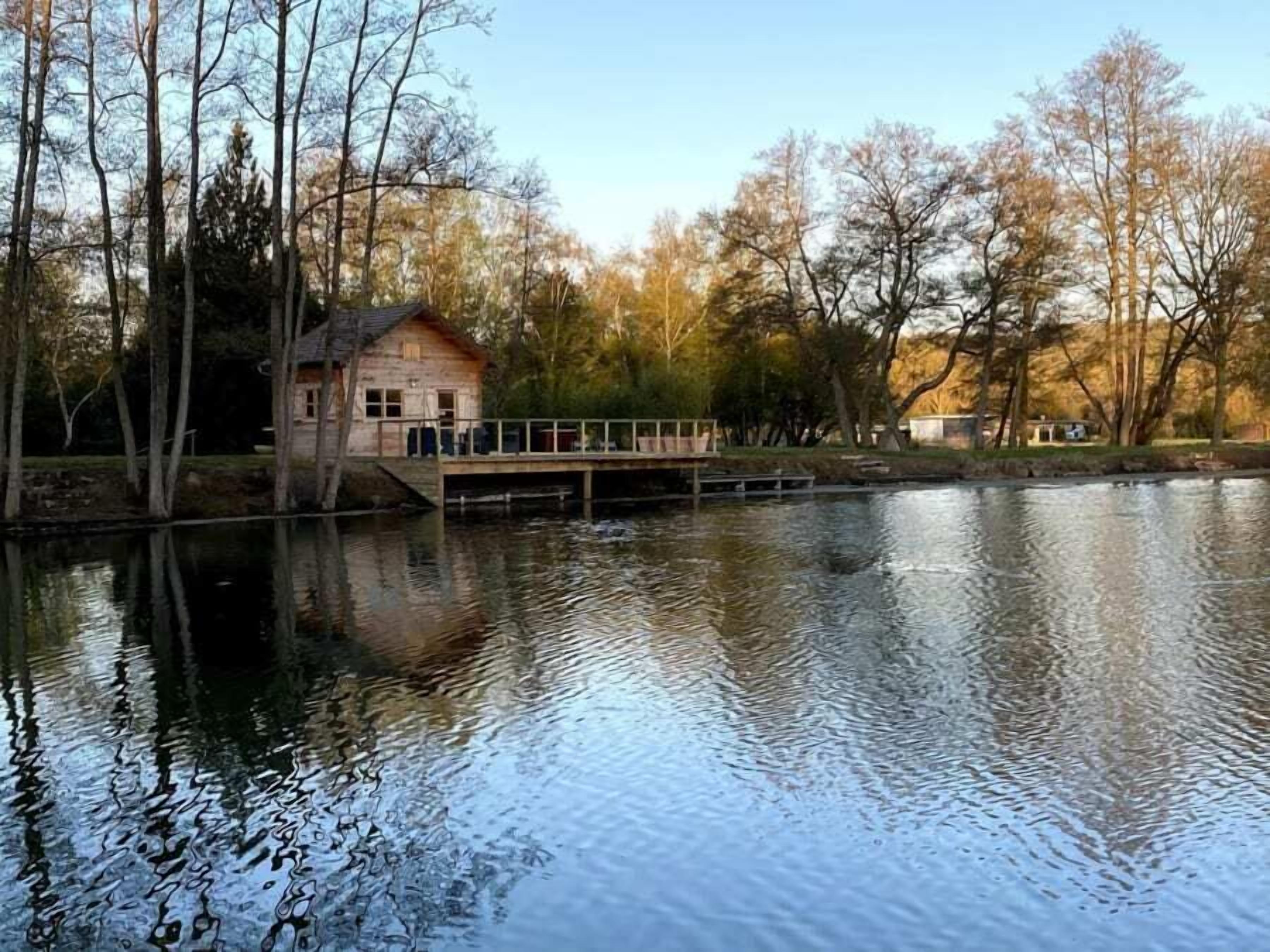 A wooden cabin by a calm lake with a dock, surrounded by trees.