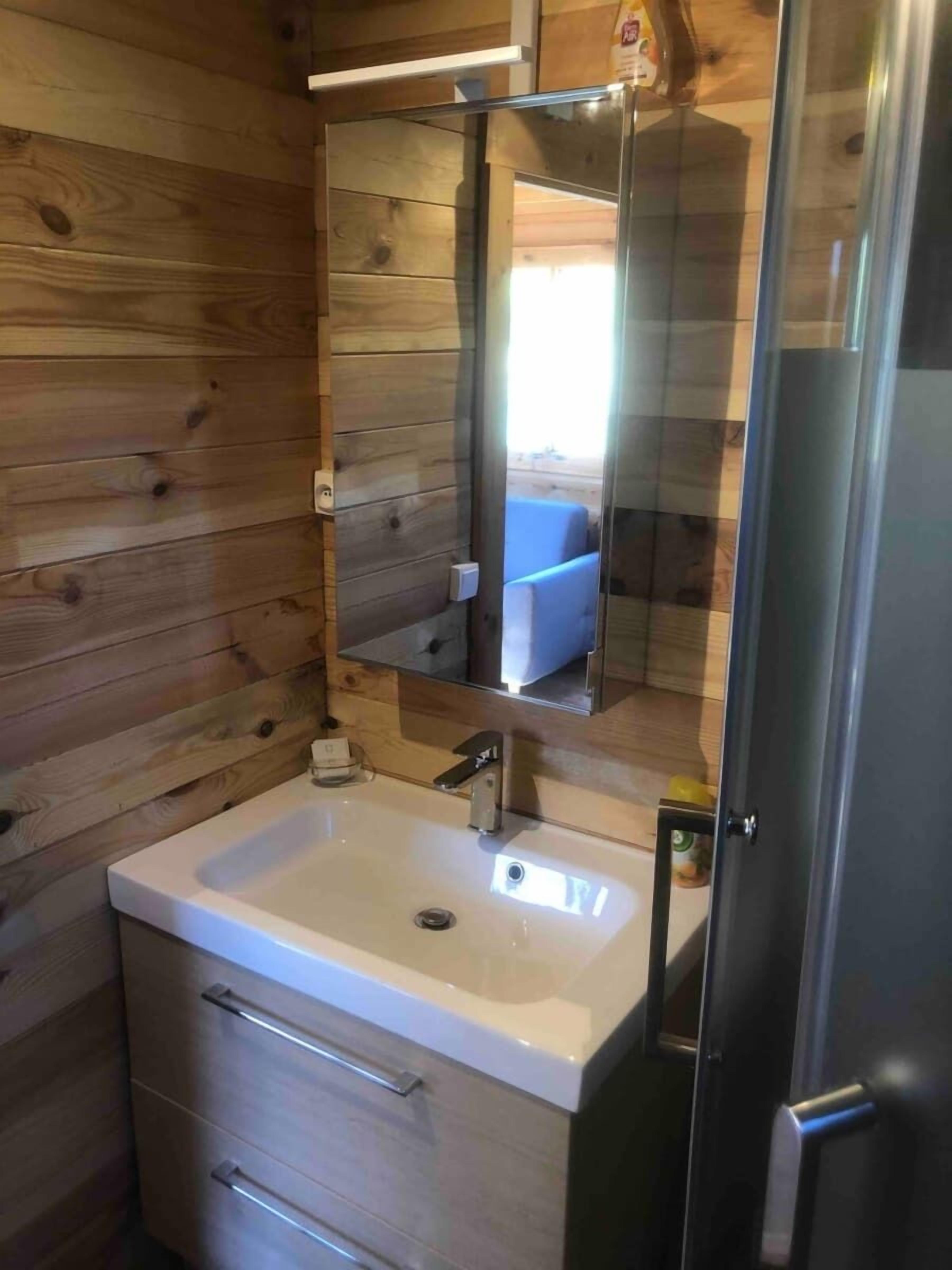 Ein Badezimmer mit Holzwänden, einem weißen Waschbecken, einem Spiegel und einer Tür.