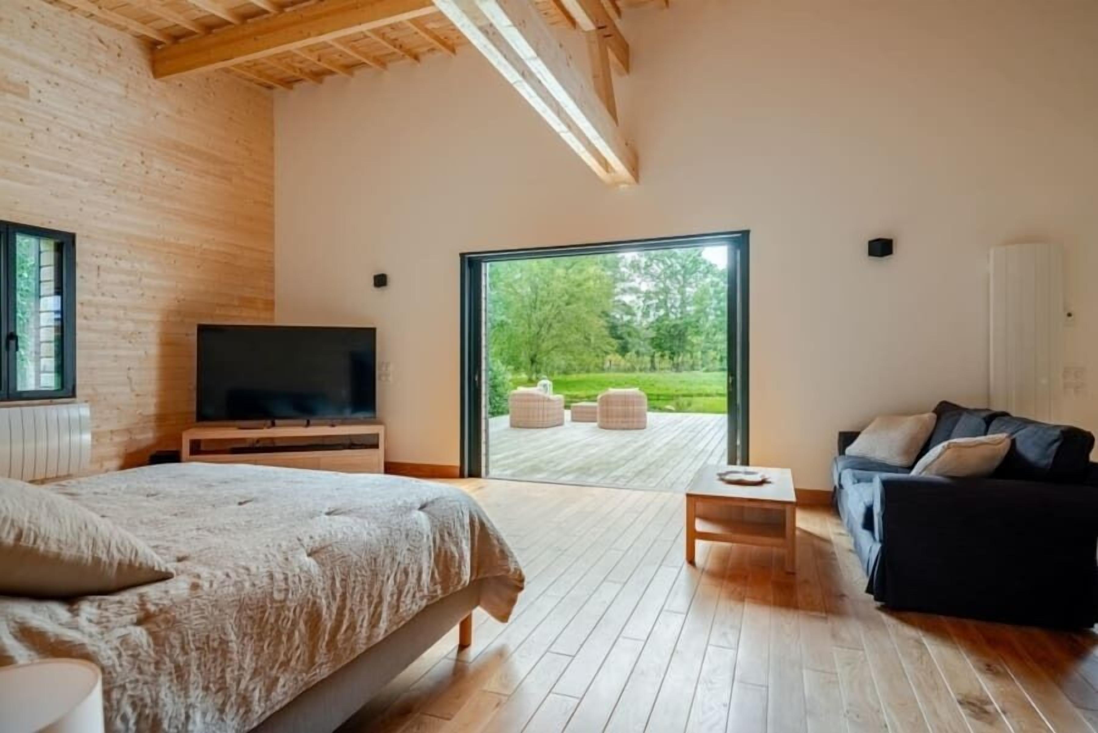Un dormitorio moderno con una cama grande, un televisor y vistas a una terraza con mobiliario exterior.