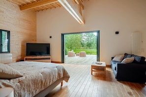 Une chambre moderne dotée d’un grand lit, d’une télévision et offrant une vue sur une terrasse avec coin salon extérieur.