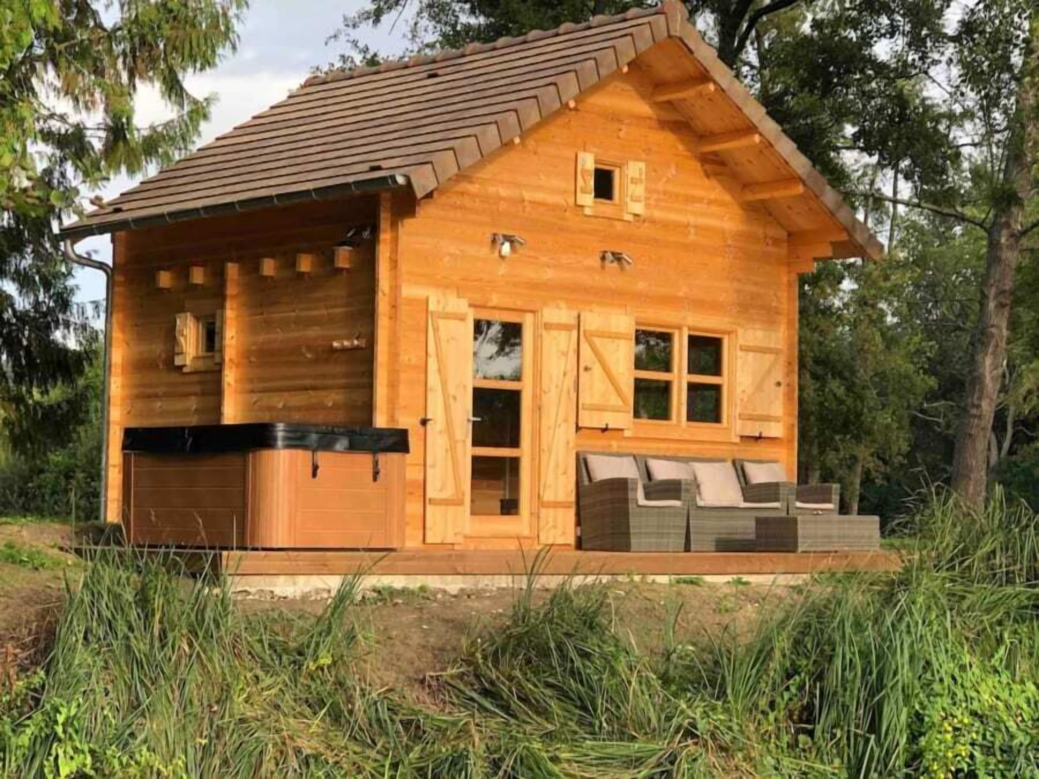 A wooden cabin with a garage, a hot tub, and a deck with outdoor seating.