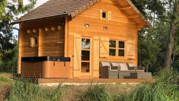 A wooden cabin with a garage, a hot tub, and a deck with outdoor seating.
