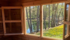 Interior de una cabaña de madera con un sofá, una ventana con vistas a un bosque y un radiador.