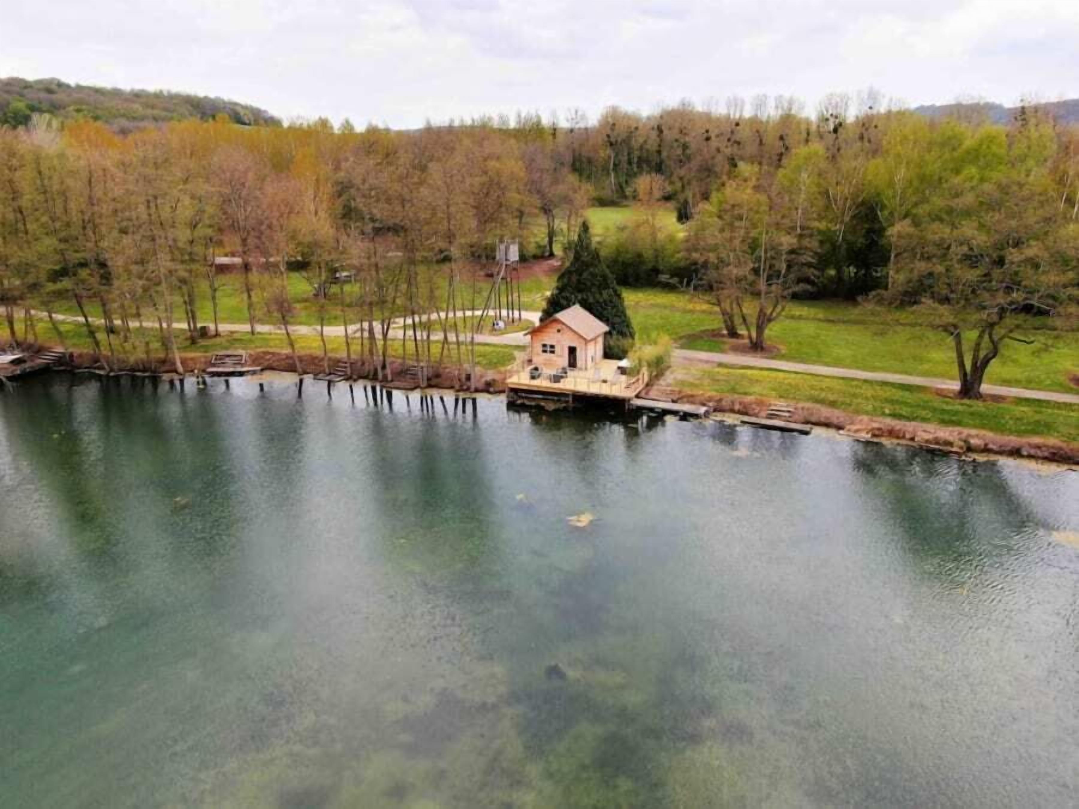 Uma cabana à beira do lago com um píer, rodeada por árvores e uma área gramada.