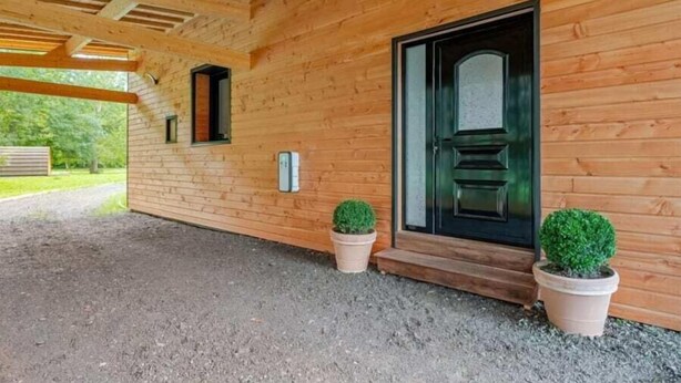 Una cabaña de madera con una puerta negra, dos macetas y un camino de grava.
