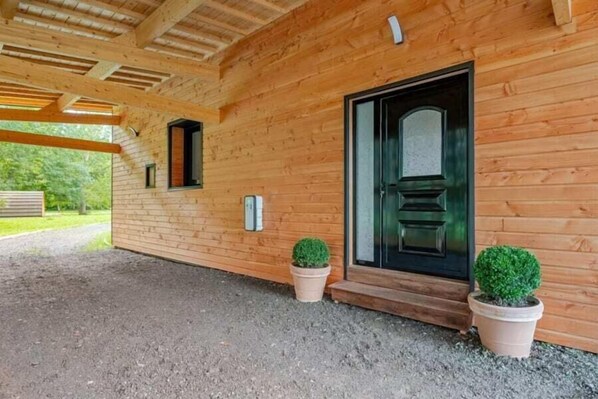 Una cabaña de madera con una puerta negra, dos macetas y un camino de grava.