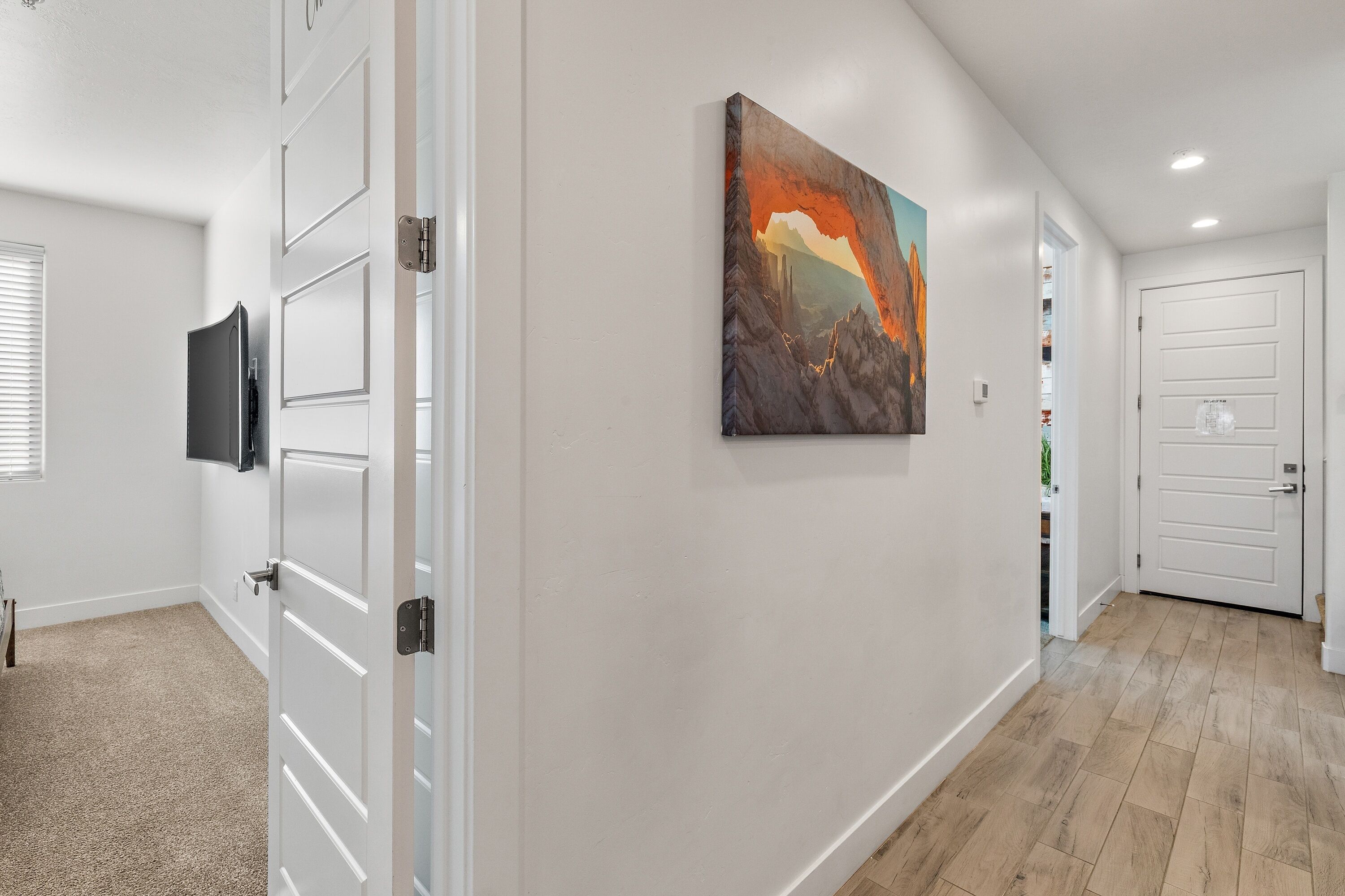A hallway with a painting, a flat-screen TV, and a door with a label.
