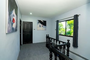 Un pasillo con una escalera, una puerta y un ventanal con cortinas.