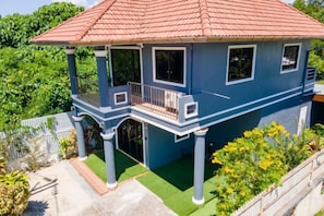 Una casa de dos pisos con un balcón, techo rojo y césped verde.